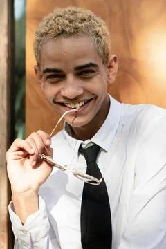 Young guy smiling at the camera playing with his glasses leaning against a .. Stock Photos