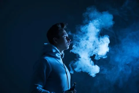 A young guy smokes a vape in the studio in neon light. Stock Photos