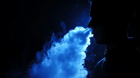 Young guy smoking e-cigarette in the dark room. Silhouette of vaper in the Video stock 106471676