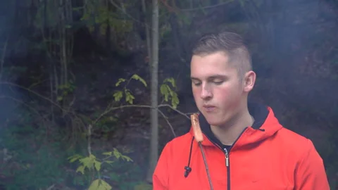 Young guy in a sporty jacket eats sausage outdoors and smiles and fun, goodies Stock Footage 195306657