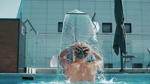 Young guy standing in the pool under the rain shower of a luxury hotel. Stock Footage 102656157