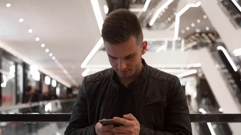 Young guy standing in shopping mall, using smartphone. 库存影片 82170261