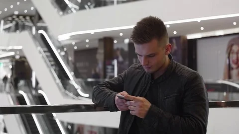 Young guy standing in shopping mall, using smartphone. Stock Footage