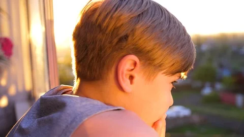 A young guy stands near the window and looks at the sunset. The sun's rays Vidéo 92532879