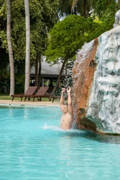 A young guy stands under artificial waterfalls in the pool on site Foto stock
