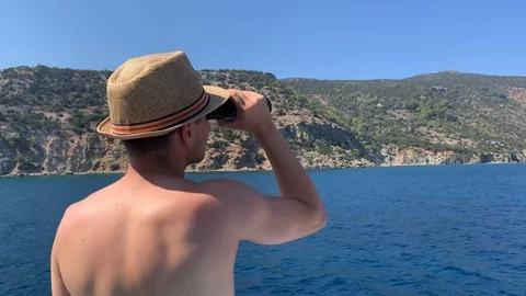 Young guy in a straw hat looks through binoculars on the seashore, cruise Video stock 125928032