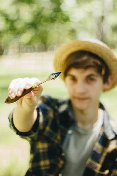 A young guy in a straw hat sits in the park in front of an easel and paints a Stock Photos