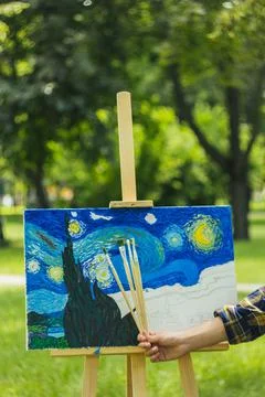 A young guy in a straw hat sits in the park in front of an easel and paints a Stock Photos
