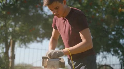 A young guy is stroiating a wooden beam with the help of an electric bank. Stock Footage 139087438