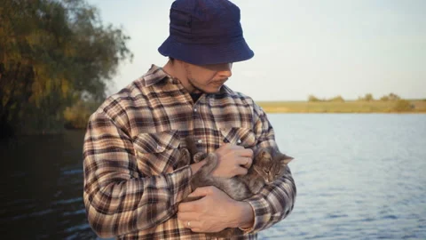 Young guy stroking a cat on the nature near the lake. Stock Footage 90581540