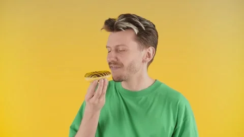 A young guy with stubble stands on a yellow background and holds a cake in his Stock Footage 241135403
