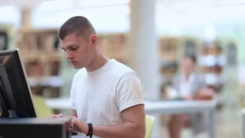 Young guy student working on computer in library Stock Footage 329391617