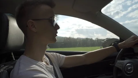 Young guy with sunglasses driving modern car by road amidst nature and forest Stock Footage 121615065