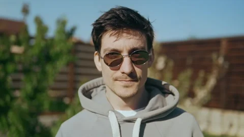 Young guy in sunglasses raises his head and looks at the camera Stock Footage 247655073