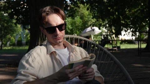 A young guy in sunglasses reading a book. Stock Footage 279745596