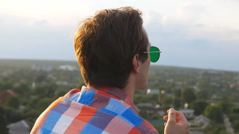 Young guy in sunglasses standing on the edge of rooftop and smoking cigarette Stock Footage 329111450