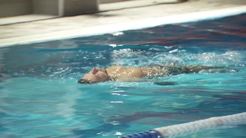 Young guy swims in the pool. along the track. on the back, a man is swimming. Video stock 134730383