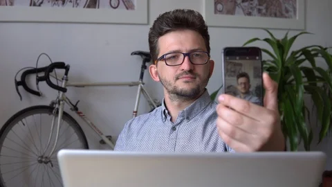 A young guy takes a selfie, sitting at the laptop against the wall with a bike Stock Footage 91981908