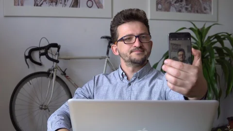 A young guy takes a selfie, sitting at the laptop against the wall with a bike Video stock 91981981