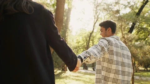 Young guy taking his girlfriend by the hand on a walk in the park. Sun shining Vídeos de archivo 219921017