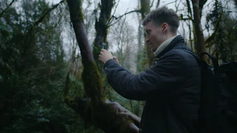 Young guy is taking photos in forest with phone, nature photography on phone Stock Footage 147493629