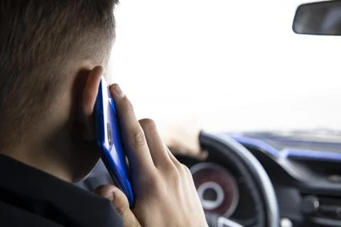 A young guy is talking on the phone while driving a vehicle. Stock Photos