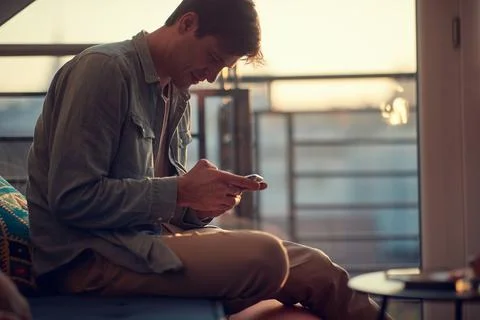 A young guy texting on the smartphone while resting at home. Man, home, leisu Stock Photos