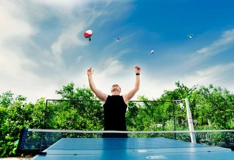 Young guy threw a ping pong racket up on a background of green trees Stock Photos