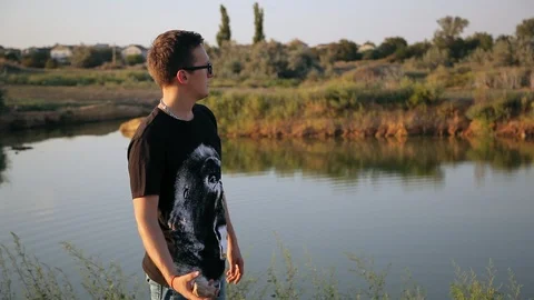 Young guy throws a stone into pond's water 5 Video stock 94442316