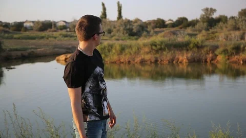 Young guy throws a stone into pond's water 4 Видео 94442323