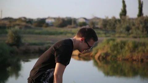 Young guy throws a stone into pond's water 3 库存影片 94442370