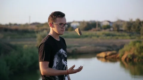 Young guy throws a stone into pond's water 2 Видео 94442384