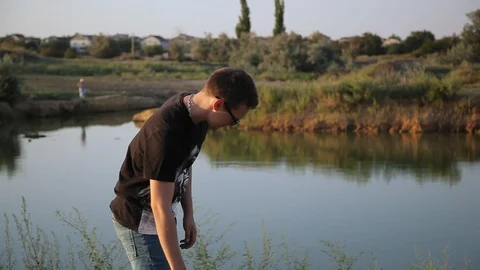 Young guy throws a stone into pond's water 1  Видео 94442386