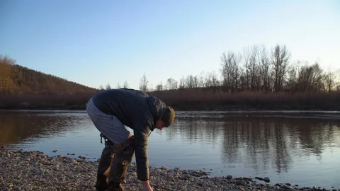 A young guy throws stones at the water. Fun on the riverbank Stock Footage 120698911