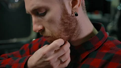 A young guy touches his beard before a haircut indoor of barbershop Stock Footage 133511044