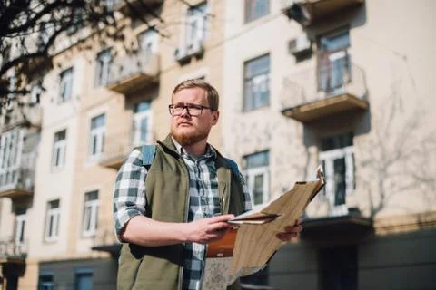 Young guy tourist is looking for a road with a map in his hands in the city. Stock Photos