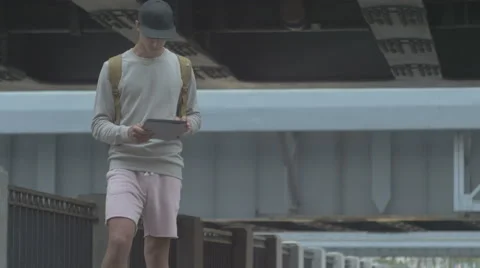 Young guy in town on a skateboard with a tablet in hand in the summer Stock Footage 65372578