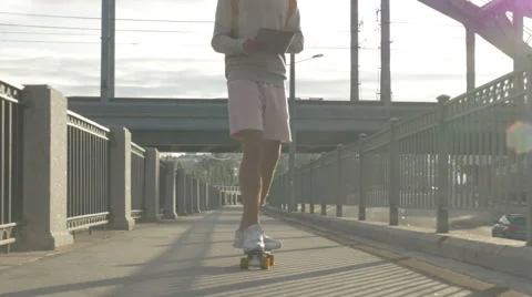 Young guy in town on a skateboard with a tablet in hand in the summer Stock Footage 65377272