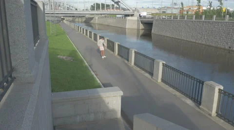 Young guy in town on a skateboard with a tablet in hand in the summer Stock Footage 65382736