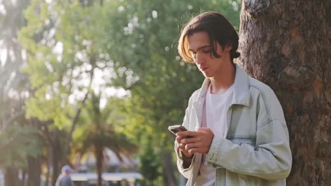 Young guy is typing a text message on a mobile phone. A young man in the pa.. Stock Footage 254657123