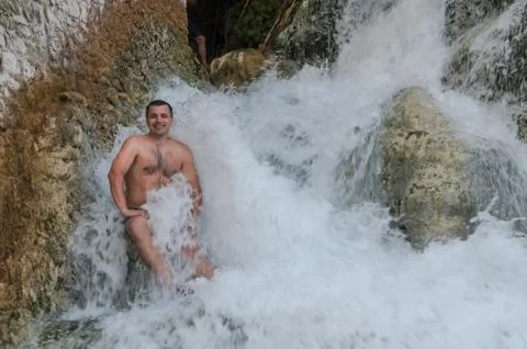 Young guy under the streams of a waterfall Stock Photos