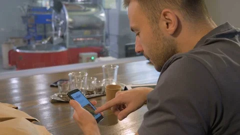The young guy uses his smartphone in the coffee house. Stock Footage 82306353