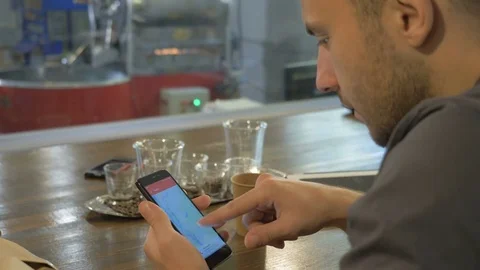 The young guy uses his smartphone in the coffee house. Stock Footage 82306862