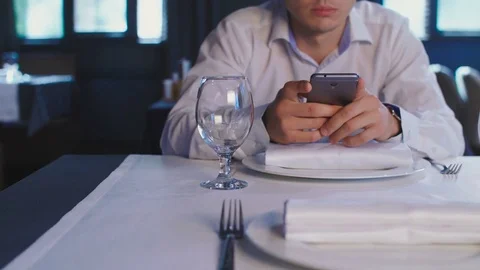 Young guy uses a smartphone while waiting for an order at a table in a Stock Footage 82469159