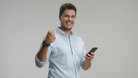 Young guy using a cell phone and gesturing happiness 스톡 동영상 77993468