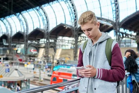 Young guy using mobile apps on smartphone standing at railway station Stock Photos