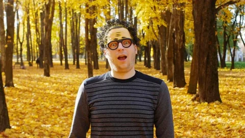 A young guy in a wacky mask on his face rejoices in autumn and looks at the Stock Footage 131090419