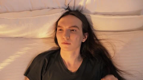 Young guy wakes up on a pillow in his bed and rubs his eyes Stock Footage 245615846