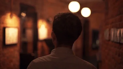Young guy is walking along the poorly lit corridor of the club. Back view Stock Footage 79357305