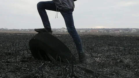 Young guy walking and stepping on the rubber tire on the burnt ground in the Stock Footage 105545350